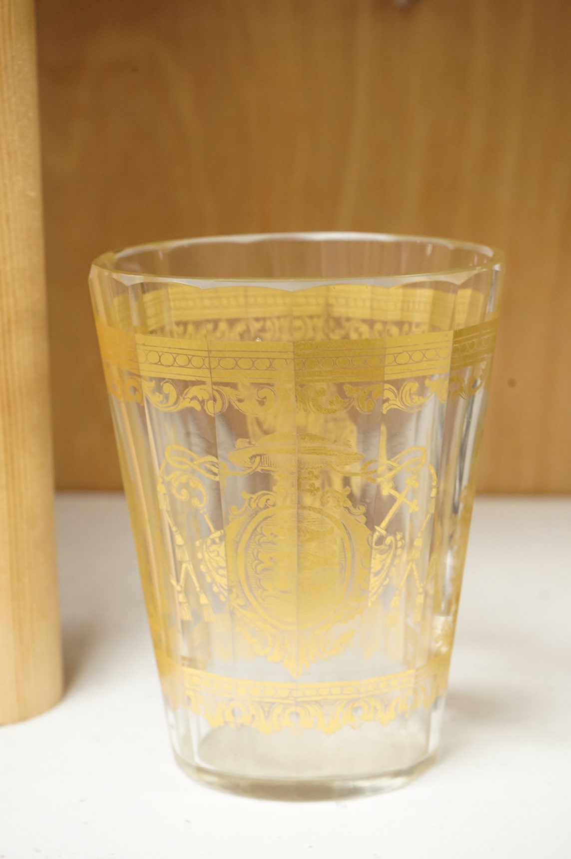 An Italian gilt-decorated and faceted beaker, inscribed Daniel Delvinis, the reverse with papal coat of arms, and a German Schwarzlot black enamelled ‘hunting’ beaker, largest 12cm (2)